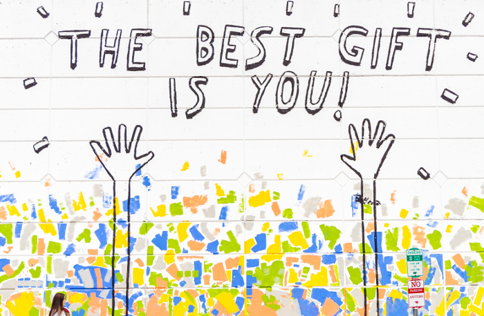 Mural callejero con decoración festiva, unas manos y el texto "the best gift is you!"
