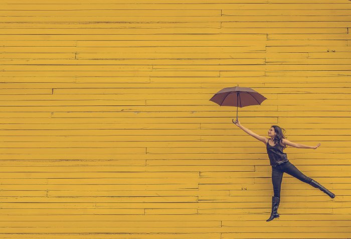Mujer con un paraguas saltando delante de una pared amarilla, color de la motivación